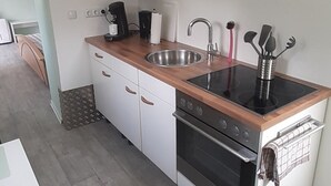 Una cocina compacta con armarios blancos, un lavamanos de acero inoxidable, un horno empotrado y una encimera de madera.