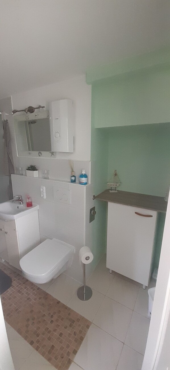 Un baño con inodoro, lavabo, espejo, armario y un pequeño estante con artículos de aseo.