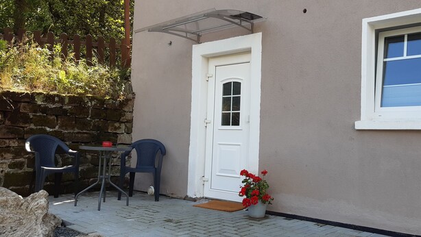 Un pequeño patio con dos sillas, una mesa, una puerta blanca y una ventana.