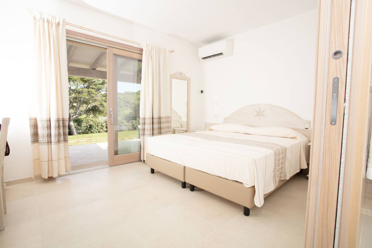 A bedroom with a bed, a sliding glass door to a balcony, and an air conditioning unit.