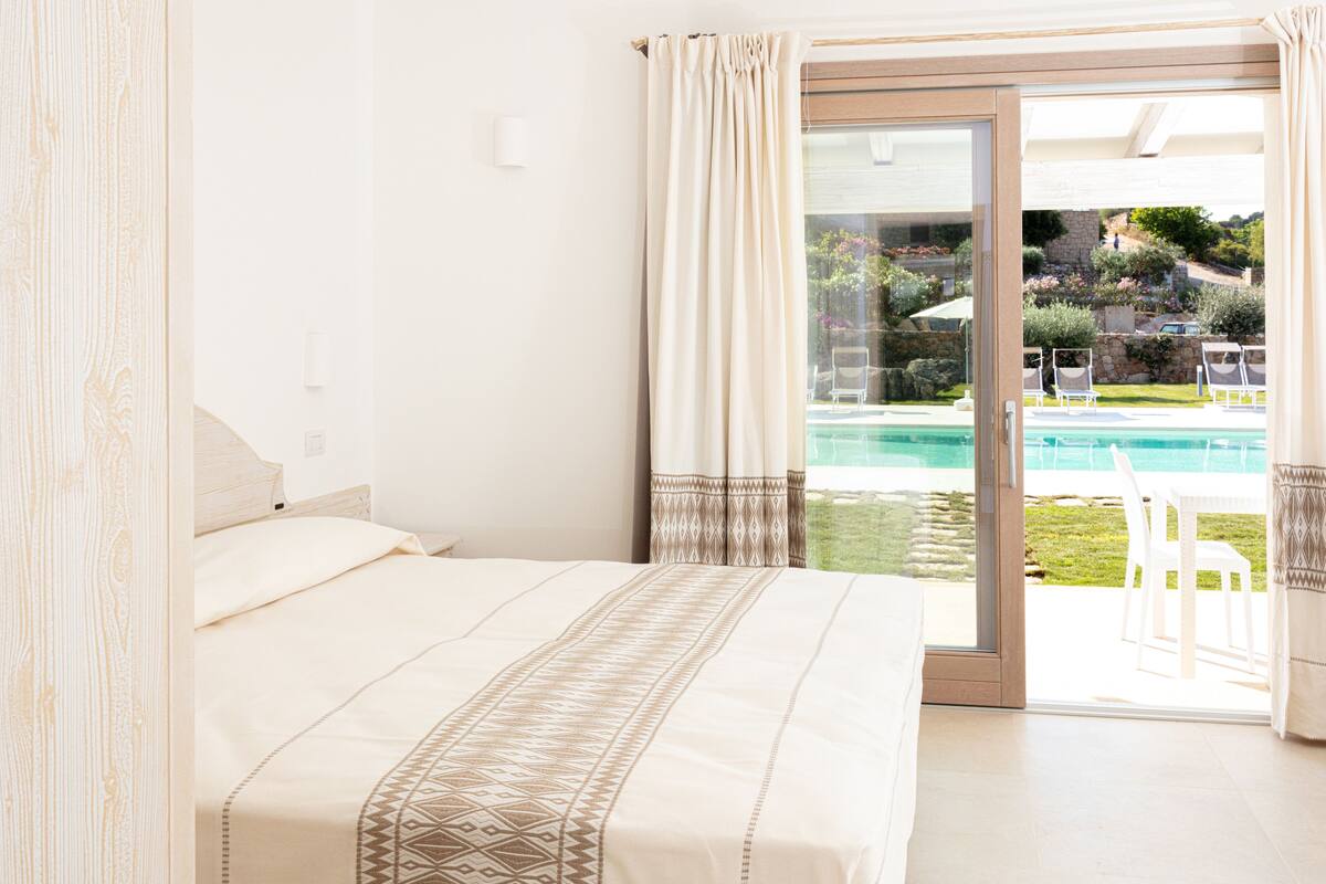 A bedroom with a large bed, a sliding glass door leading to a pool area.