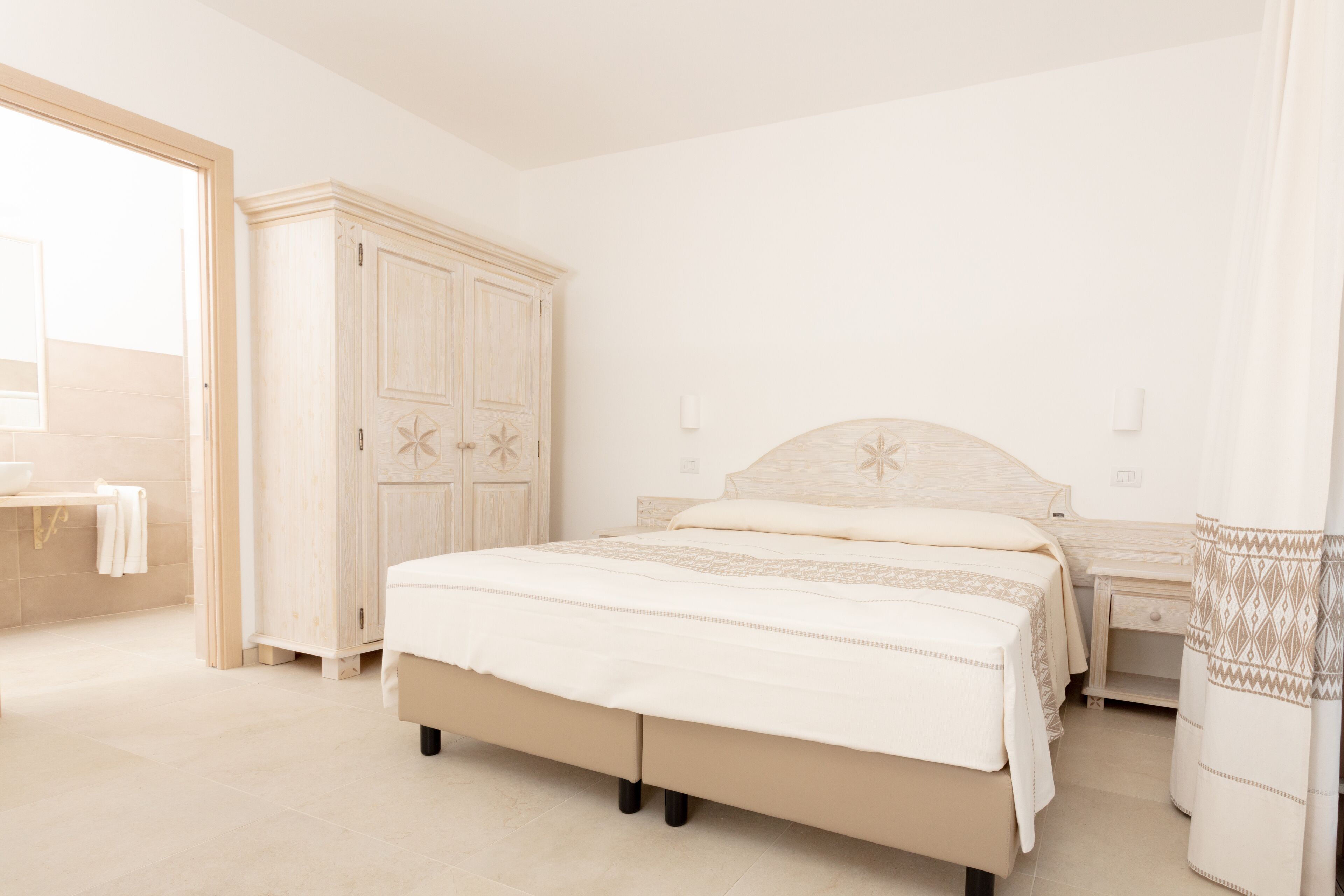 A bedroom with a bed, bedside tables, a wardrobe, and a bathroom visible through an open door.
