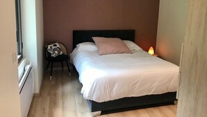 Un dormitorio con cama, una silla, una mesita de noche y una ventana.