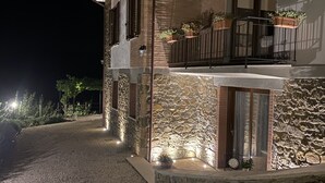 A building with a stone facade, a balcony with potted plants, and a gravel driveway. - Podere Belsogno-apartment rose garden (Montalcino)