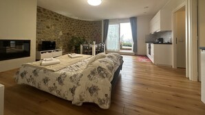 A bedroom with a large bed, a TV, a stone wall, a dining area, and a kitchen. - Podere Belsogno-apartment rose garden (Montalcino)
