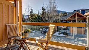 Una terraza de madera con dos sillas y una mesita, con vistas a un paisaje nevado con casas y árboles.
