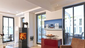 A modern living room with a fireplace, a red cabinet, and a large window with a view of the beach. - Baltic Cloud, Villa Augustine (Binz)