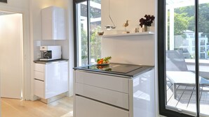 A modern kitchen with white cabinetry, a built-in oven, and a window overlooking a balcony. - Baltic Cloud, Villa Augustine (Binz)