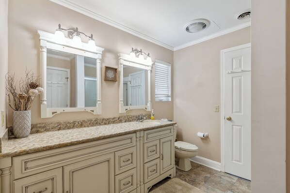 A bathroom with a beige wall, a white door, a vanity with a mirror, a toilet, and a sink. - Driftwood Too - 4 Bed/2 Bath Home on the Channel in Cherry Grove (North Myrtle Beach)