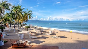 Un resort frente al mar con sillas de descanso, sombrillas y una terraza de madera con vista al océano.