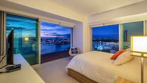 Una habitación de hotel moderna con una cama grande, un escritorio con computadora y vistas a un paisaje urbano de noche.