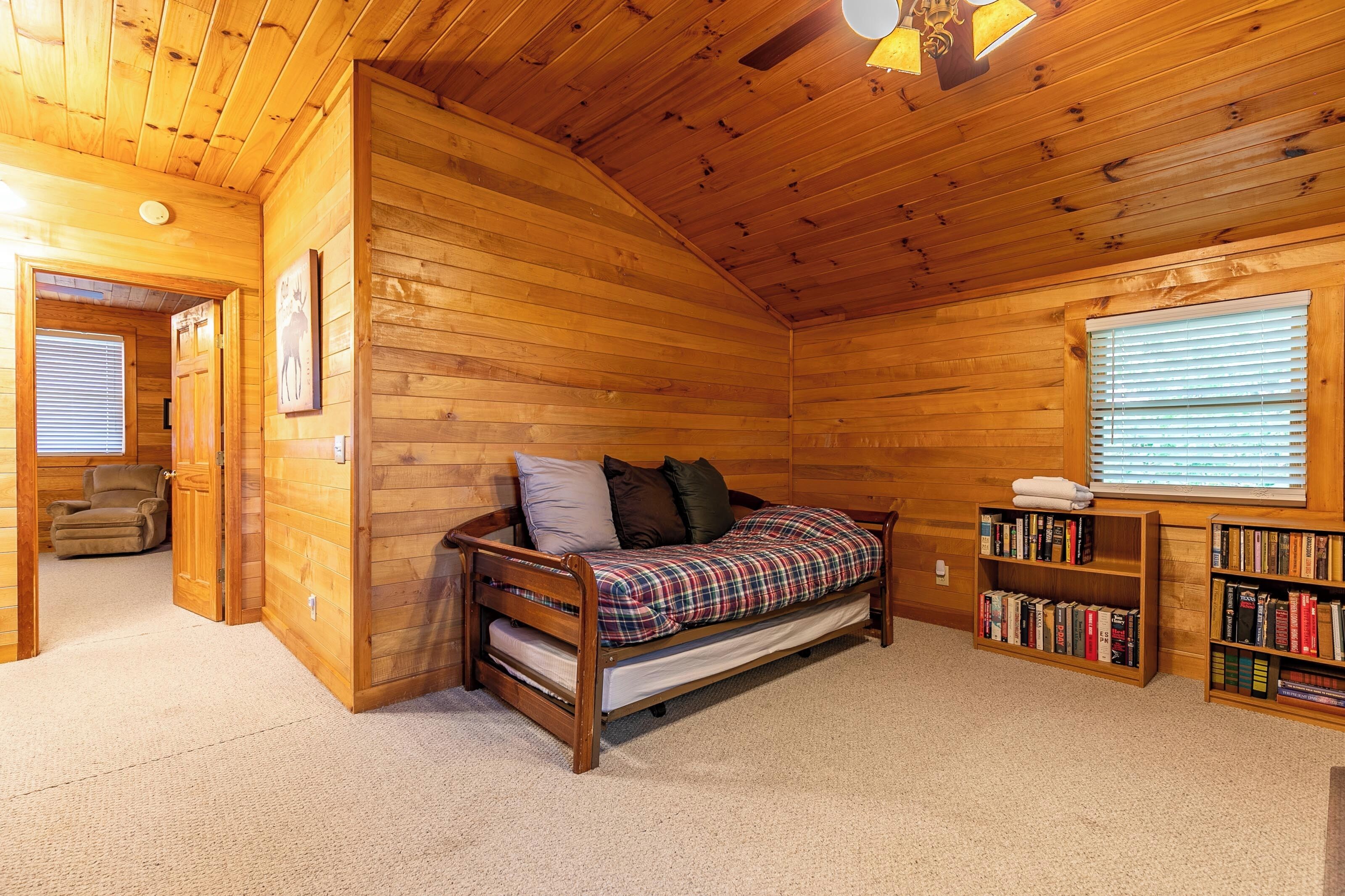 Um quarto acolhedor de cabana de madeira com cama no mezanino, um espaço de leitura com estantes e uma janela com persianas.