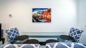 A modern room with a glass table, two patterned chairs, and a vibrant cityscape painting on the wall.