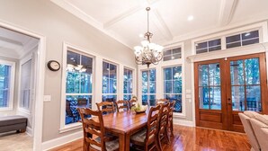 A dining room with a wooden table and chairs, large windows, and a chandelier. - Luxury Lakefront Getaway on Beautiful Lake Sinclair (Eatonton)
