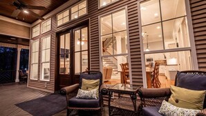 A spacious deck with wicker furniture and a glass table, overlooking a well-lit interior with a staircase and kitchen. - Luxury Lakefront Getaway on Beautiful Lake Sinclair (Eatonton)