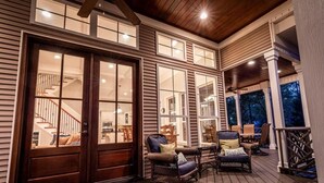 A covered porch with wicker furniture, a wooden door, and a view of the interior. - Luxury Lakefront Getaway on Beautiful Lake Sinclair (Eatonton)