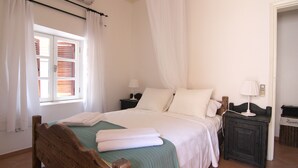 Un llit ben fet amb un estovat verd, almoines blanques i una tovallola blanca plegada al peu del llit. Hi ha una taula de nit amb una làmpada i una cistella petita amb la inscripció 'Laundry'.