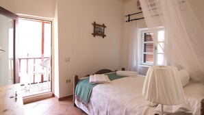 Un dormitori amb un llit, una finestra amb cortines, una taula de nit i una cadira a prop de la finestra.