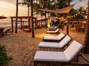 Un espace de détente aménagé sur la plage, avec des chaises longues en bois et un auvent.