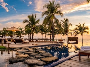 A poolside area with lounge chairs, palm trees, and a view of the ocean.