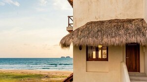 Una propiedad frente al mar con una estructura de techo de paja, una escalera que lleva a una puerta de madera y vistas al océano.
