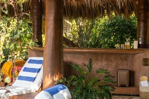 A sunlit lounge area with a thatched roof, a lounge chair, a small table, and a potted plant. - Casamar, beach front estate on Troncones Point (La Majahua)