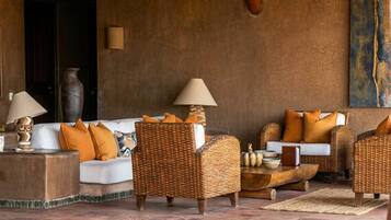 A cozy lounge area with wicker furniture, white sofas, and orange cushions.