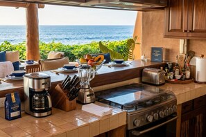 A kitchen with a view of the ocean, equipped with a coffee maker, blender, toaster, and stove. - Casamar, beach front estate on Troncones Point (La Majahua)