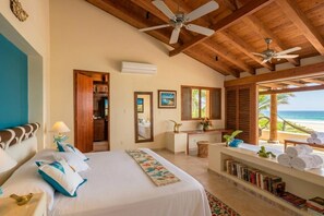 A hotel room with a bed, a desk, a chair, a bookshelf, and a view of the beach. - Casamar, beach front estate on Troncones Point (La Majahua)