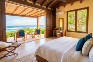 A bedroom with a large bed, a desk, and a view of the ocean.