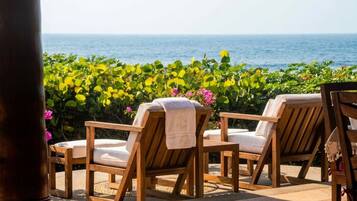 Two wooden lounge chairs with towels, positioned on a patio with a view of the sea and lush greenery.