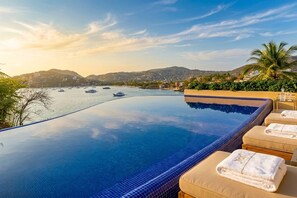 A infinity pool with a view of boats and hills. - KauKan B7 Luxury Condo with Breathtaking View (Zihuatanejo)