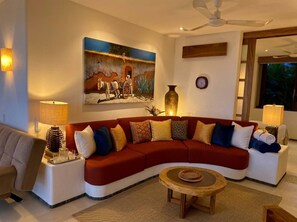 A living room with a red sectional sofa, a round coffee table, and a painting on the wall.