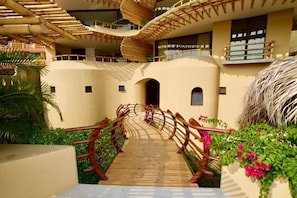 A wooden pathway leading to a building with multiple balconies and a thatched roof structure. - KauKan B7 Luxury Condo with Breathtaking View (Zihuatanejo)