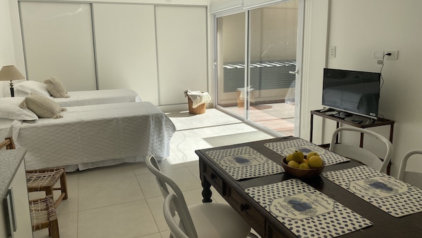 A hotel room with two beds, a dining table with placemats, a TV, and a balcony with a view. - Divino Loft - Mas Centrico Imposible (Salta)