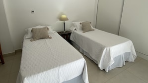 A room with two single beds, a bedside table with a lamp, and a plain white wall. - Divino Loft - Mas Centrico Imposible (Salta)