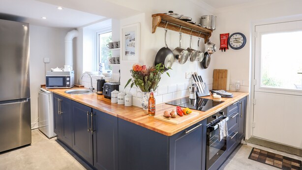 A modern kitchen with a wooden countertop, stainless steel appliances, hanging pots, and a 'Gone to the Beach' sign. - Silva (Beaumaris)