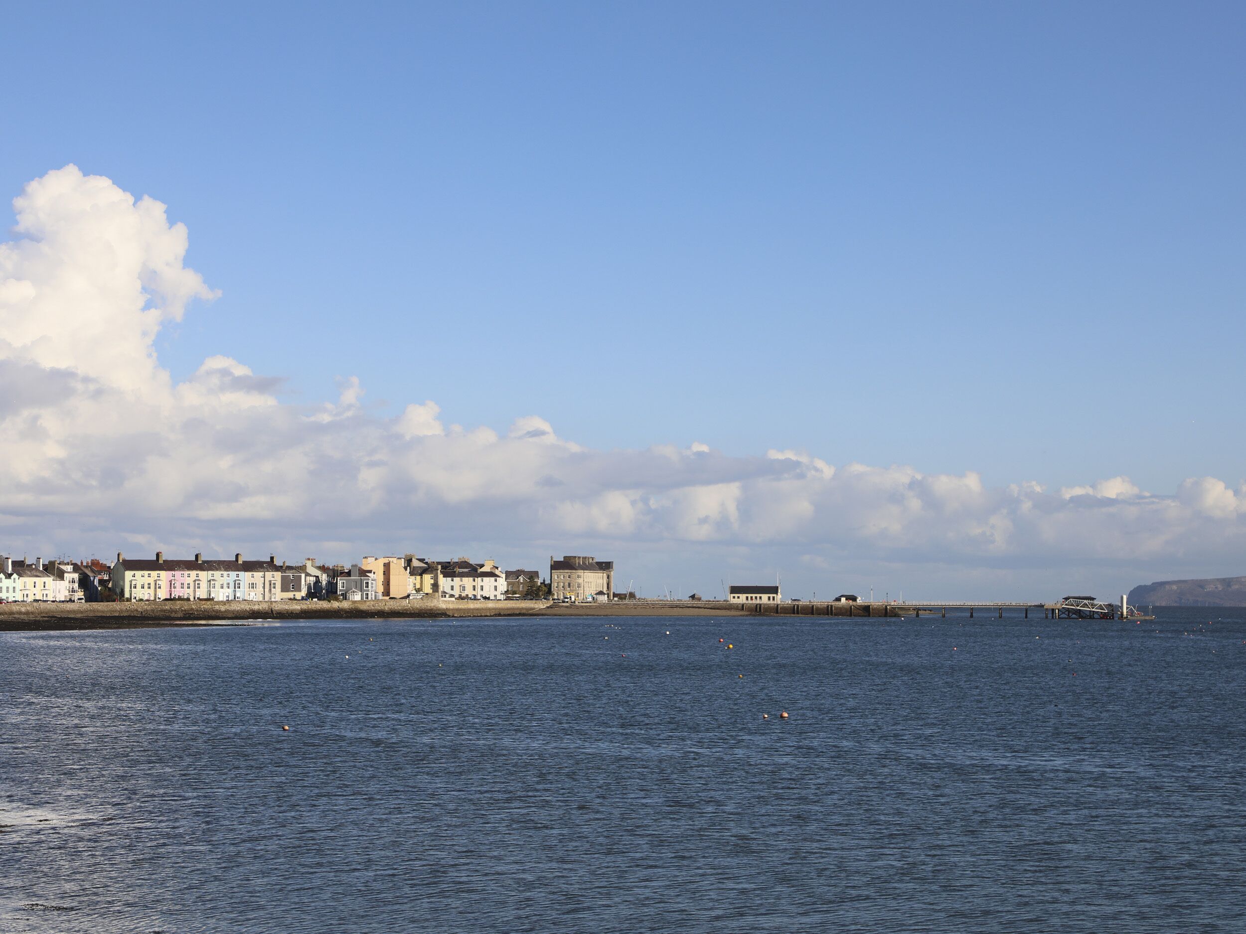 En kuststad med historiska byggnader längs strandpromenaden, en bro och en klar himmel.