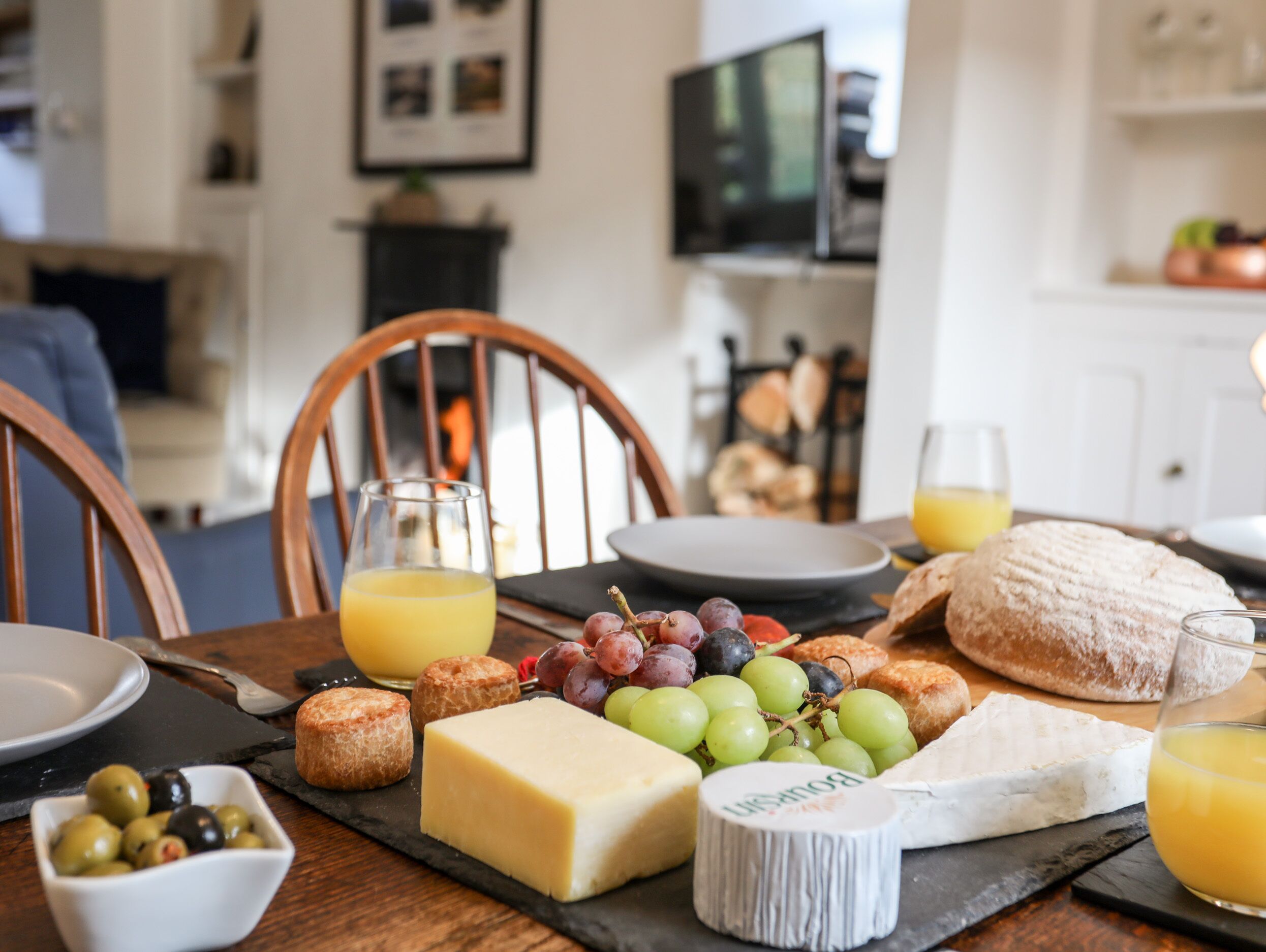 A breakfast setting with cheese, grapes, bread, and juice on a wooden table.