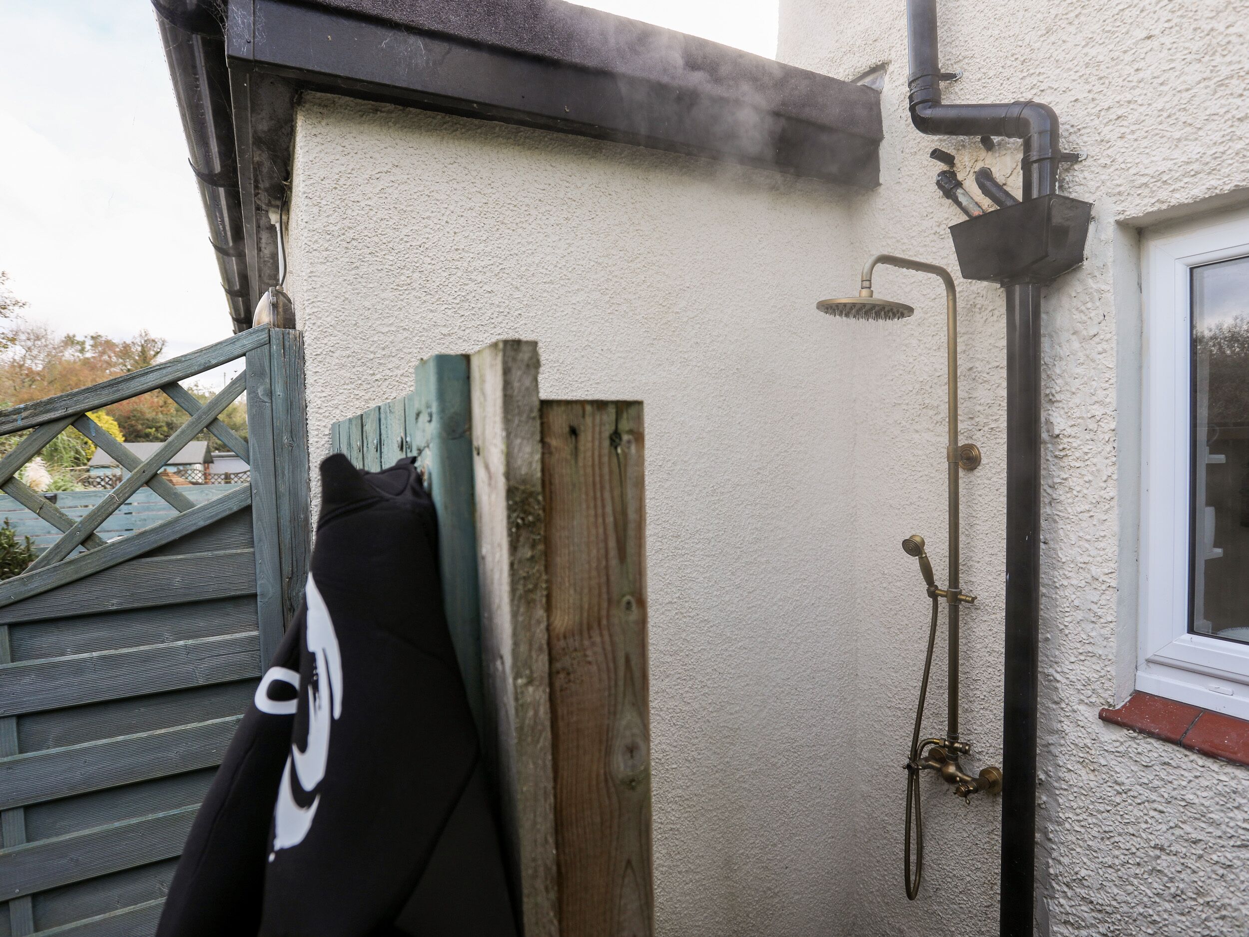 A wooden gate, a metal showerhead, and a window with a white frame.