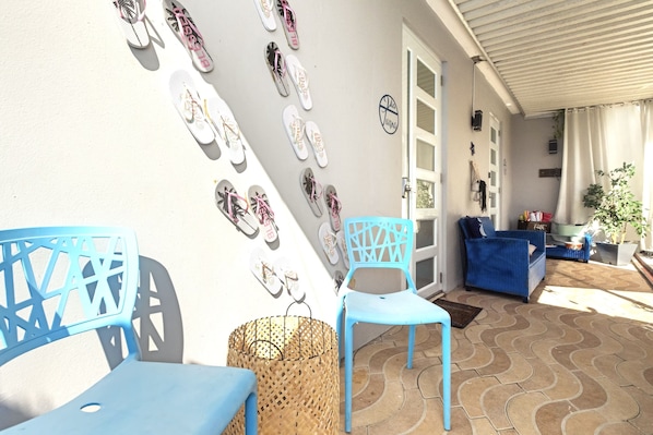 Un'area patio con sedie e tavoli blu, un cesto di vimini e un muro decorato con ciabatte.