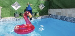 Una piscina con un flotador de flamenco, una botella decorativa azul y un letrero que dice 'hogar' en una pared verde.