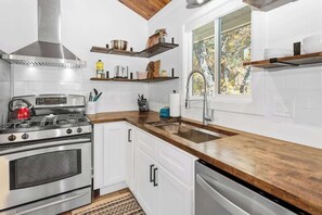Una cucina moderna con mobili bianchi, elettrodomestici in acciaio inossidabile, piani di lavoro in legno e una finestra vista alberi.