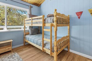 A bunk bed in a room with light blue walls, a wooden floor, and a window overlooking trees. - Bear Family Den • Game Room • Fenced • RV Parking (Big Bear)