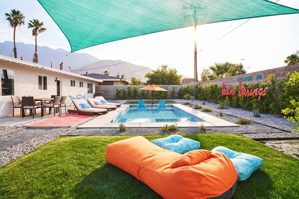 A backyard with a swimming pool, outdoor furniture, and a 'Welcome to Palm Springs' sign.