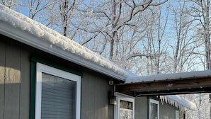 Eine Holzhütte mit großen Fenstern, einer Veranda und einem mit Schnee bedeckten Dach.