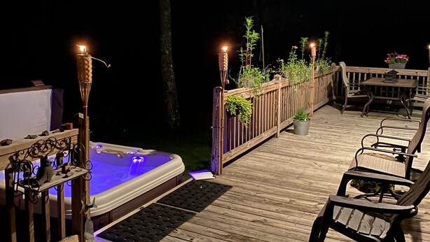 Eine Holzterrasse mit Whirlpool, Liegestühlen und Tiki-Fackeln.