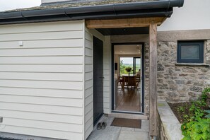 Una casa moderna con puerta principal de madera, pared de piedra y un patio con mesa y sillas.