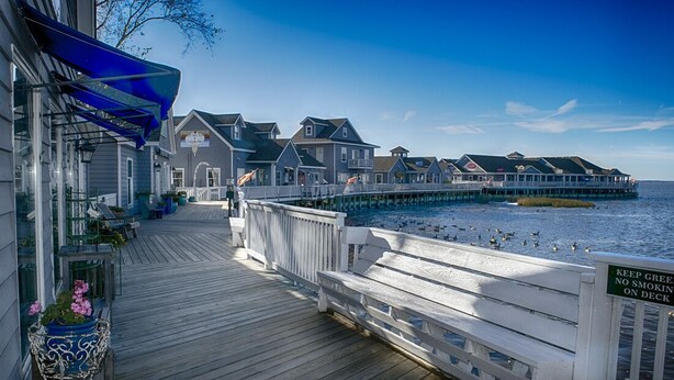 A wooden pier extending into a body of water with a row of houses on the other side. - BIS-Duck Resort - 2BR/2.5BA - Great Beach and Pools! (Duck)