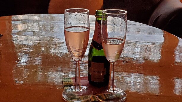 Een tafel met twee glazen wijn en een fles, voor een bank met uitzicht op een wateroppervlak.
